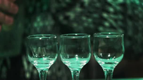 Detailní záběr. Tři skleničky v baru, chlap otevře láhev vodky v pozadí — Stock video