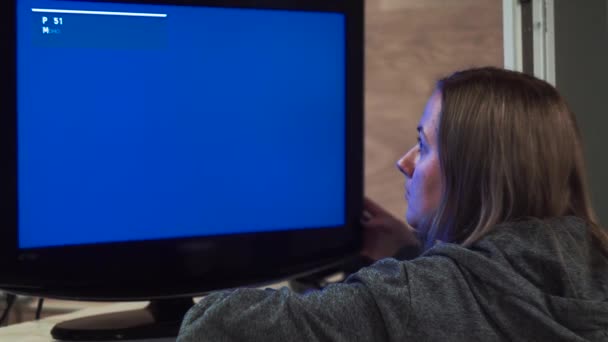 La chica mira la pantalla azul, el monitor de TV, cambia de canal — Vídeos de Stock