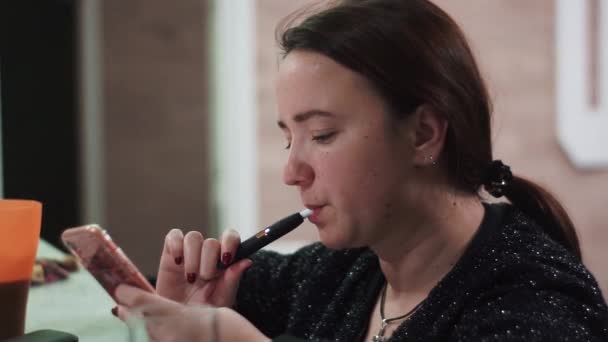 Девушка курит iqos, электронные сигареты, используя смартфоны смс обмена сообщениями в социальных сетях наслаждаясь мобильной технологии расслабляющий — стоковое видео