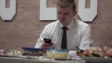 guy at a holiday sitting at a table with food, looking at a smartphone