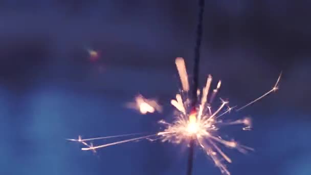 Burning orange flame of sparklers with sparks in the afternoon, morning on the street, outdoors in defocusing, on a blue background of the river, the other shore. — Stock Video