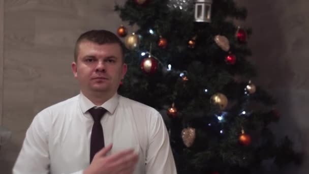 Guy wholeheartedly wishes happy new year, holidays audience. Christmas tree background — Stock Video
