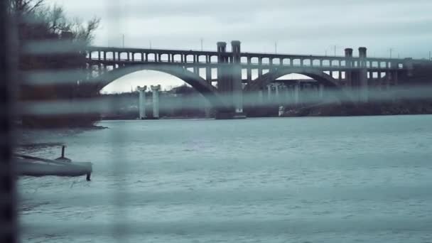 Shooting from room, through blinds street, river, bridge, city, cars, unfinished object, fittings, trees. — Stockvideo