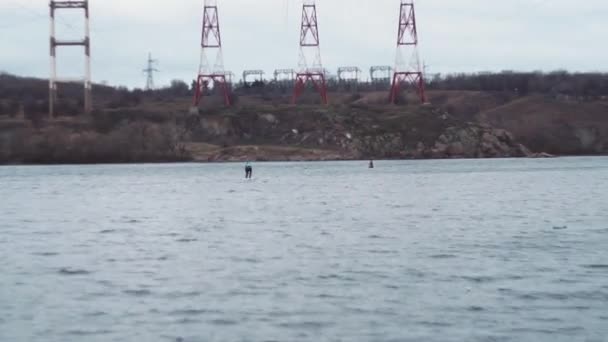 Overall plan. A man, floating on SUP, in a jacket, on a river in winter. — Stockvideo