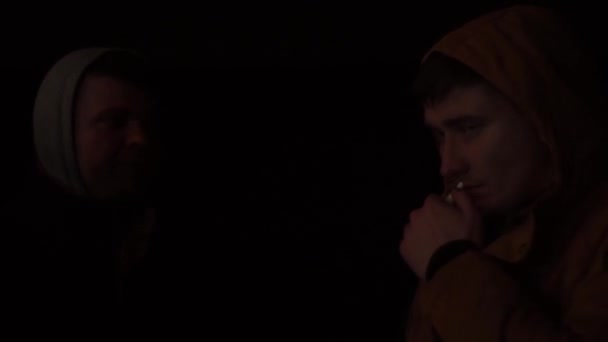 Man bullebak in een jas met een kap op een donkere achtergrond, 's nachts op straat — Stockvideo
