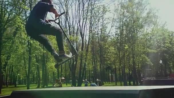 젊은 남자가 스포츠 스쿠터 도시 스케이트 공원에서 트릭을 하고 있어요. 그는 기울어진 경사로로 뛰어내렸다. 극단적 인 스포츠는 청소년들 사이에서 매우 인기가 있다. — 비디오