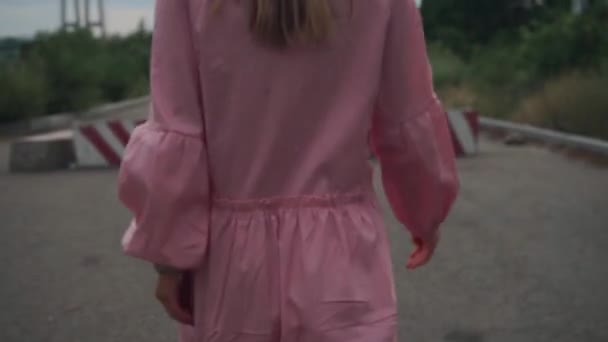 Uma menina de vestido rosa passa por blocos de concreto, estradas, carros, cidades — Vídeo de Stock