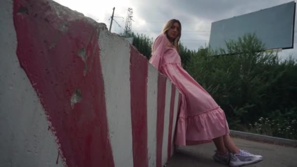 Menina séria em um vestido rosa começa a rir, outdoor em branco no fundo — Vídeo de Stock