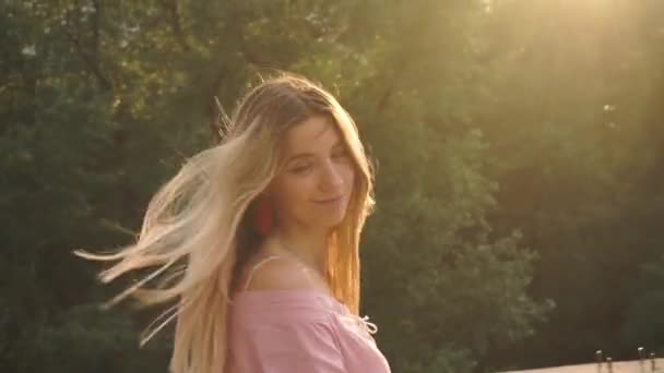 Ein fröhliches, fröhliches, lächelndes Mädchen in einem Kleid schreitet auf der Brücke, der Sonne gegenüber — Stockvideo
