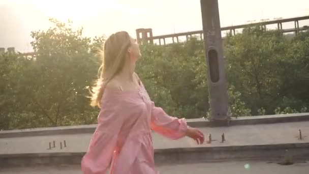 Une fille heureuse, joyeuse et souriante dans une robe marche sur le pont, en face du soleil — Video