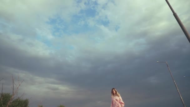 Hermosa modelo en vestido caminando hacia la cámara, cielo oscuro y nublado en el fondo — Vídeos de Stock