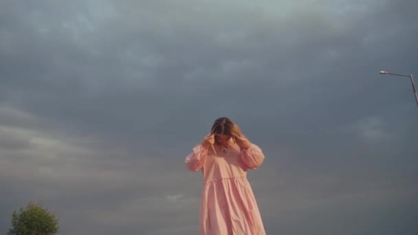 Beautiful model in dress walking towards camera, dark, cloudy sky on background — Stock Video