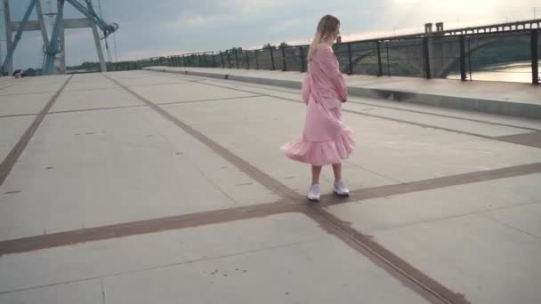 Menina alegre em um vestido girando em torno de seu eixo em uma ponte de concreto, ferro — Vídeo de Stock