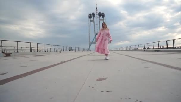 Дівчина в сукні, жарти, дурні навколо, сміється на мосту, будівельному майданчику — стокове відео