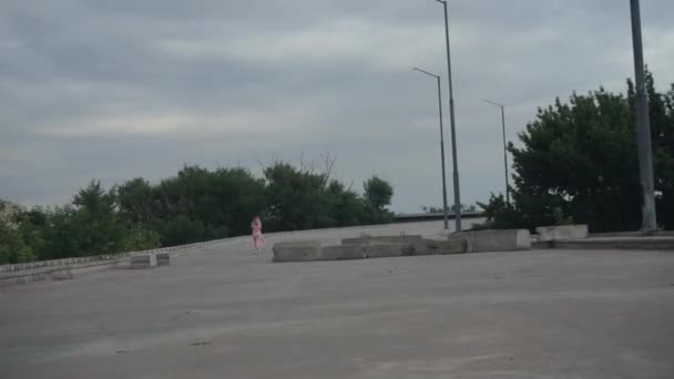 Uma menina caminha ao longo de uma estrada de concreto deserta, uma ponte inacabada — Vídeo de Stock