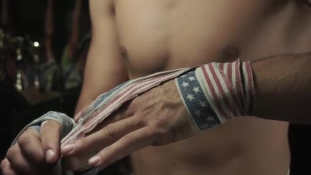 Boxer com tronco nu envolve ligaduras com bandeira americana seu crepúsculo mão esquerda — Vídeo de Stock