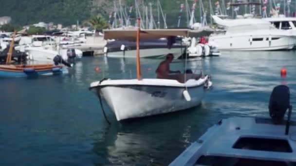 BUDVA, MONTENEGRO - AUGUST 22, 2019: A man boat, under a canopy, swims up to the pier, against the background of yachts, sea, mountains — Stock Video