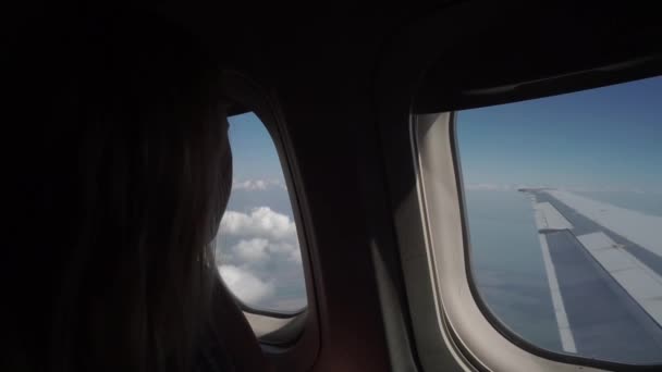 Young girl travels by plane, sits by window and enjoys view through porthole. — Stock Video