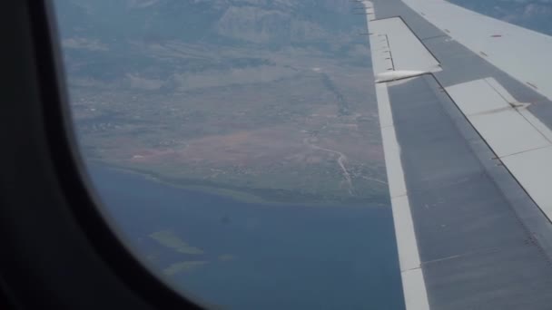 Sayap pesawat di udara. Down di tanah yang jauh, pantai darat, laut di latar belakang — Stok Video