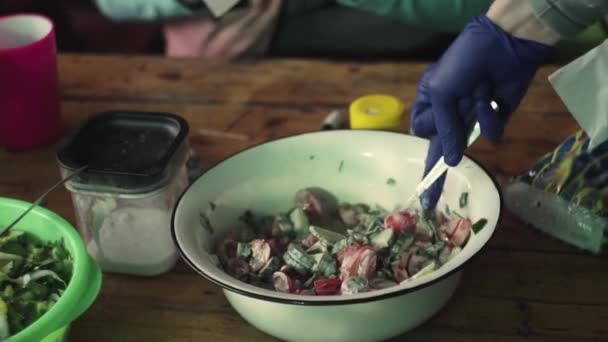 Рука в перчатке смешивает салат из огурцов, помидоров, трав, сметаны, в стране — стоковое видео