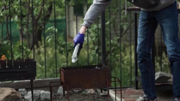 El tipo con guantes vierte leña en la barbacoa, líquido de ignición en el campo — Vídeo de stock