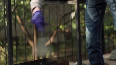 Yakın plan. Ateşe körükle gitmek, kömürden kıvılcımlar saçmak, mangalda yakacak odunla kürek kullanmak.