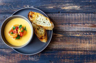 Ahşap arka planda ızgara karidesli krem peynir çorbası.