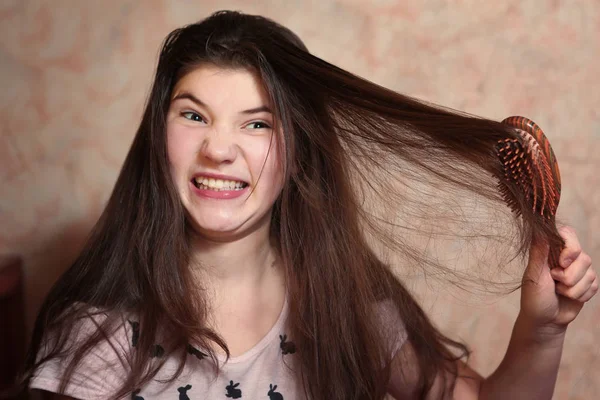 Menina adolescente tentar pentear seu longo cabelo grosso escuro — Fotografia de Stock