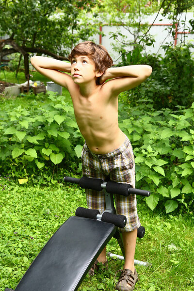 Мальчик отрабатывает отжимания на тренажере под открытым небом
