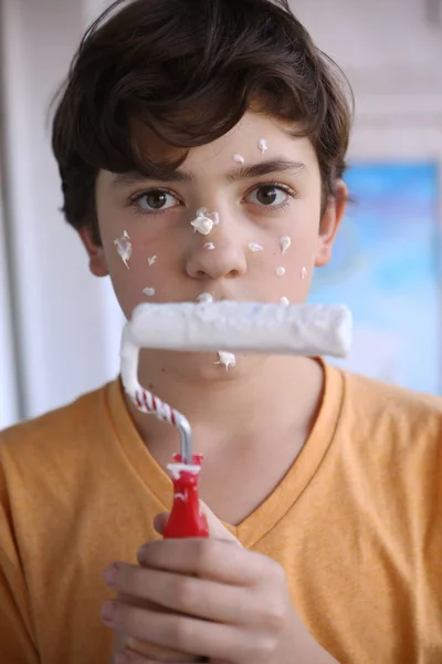Усміхнений хлопчик-підліток з білою фарбою ролик і брудне обличчя роблять перефарбування — стокове фото
