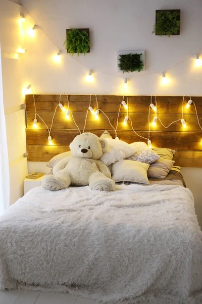 Białe łóżko z misia z girlandy świątecznej dekoracji światła — Zdjęcie stockowe
