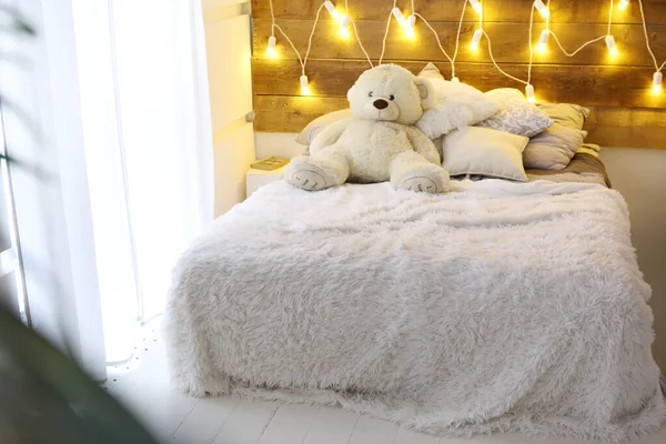 Белая кровать с плюшевым медведем и световым украшением из гирлянд — стоковое фото