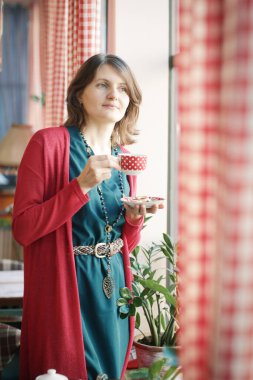 Kafe penceresinden çay fincanı portresi taşıyan genç sarışın kadın. Yakın plan.