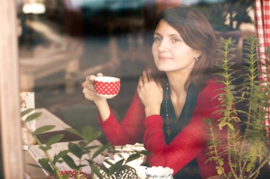 Kafe penceresinden çay fincanı portresi taşıyan genç sarışın kadın. Yakın plan.