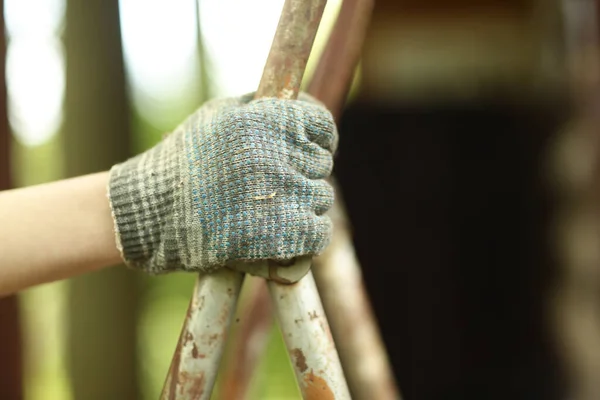 close up photo of human hand in glove holding ladder on country house background