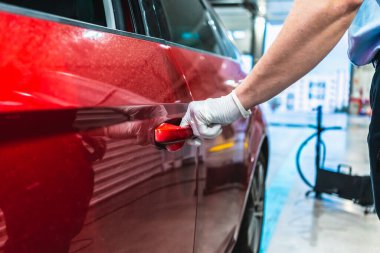 Beyaz tenli genç bir teknisyen, virüsün yayılmasını önlemek için maske ve eldivenle korunan bir aracın kapısını açıyor.