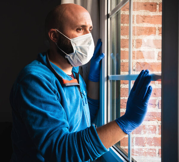 Sick man with mask and medical gloves looking through the window, probably infected by coronavirus and self isolated