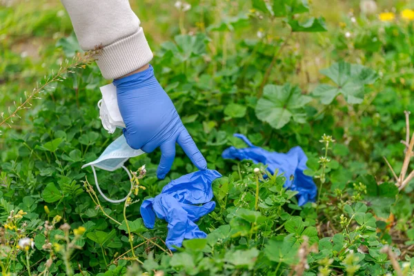 El temizleme eldiveni, cerrahi maske ve çimlerin üzerinde duran çöp.