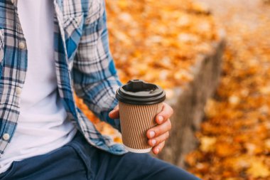 Paper cup of coffee in man hand in the autumn park