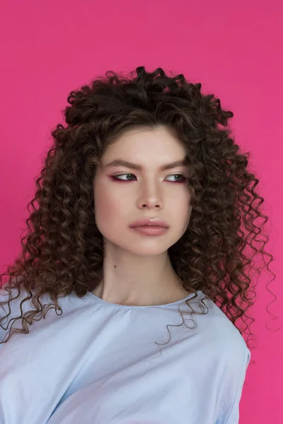 Young beautiful model with afro curls hairstyle wearing blue blouse on pink background