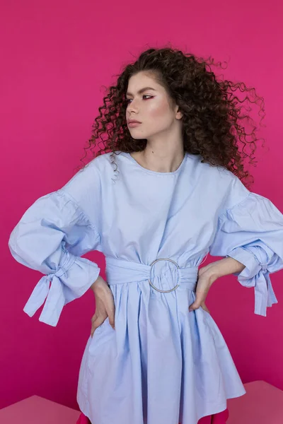 Young beautiful model with afro curls hairstyle wearing blue blouse on pink background