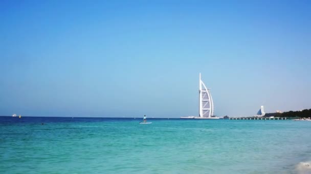 Dubaj, Spojené arabské emiráty - 20. ledna 2018. Surfař a Burj Hotel al Arab na pozadí. Vlny na pláži Al Sufouh. Moře. Perský záliv. — Stock video