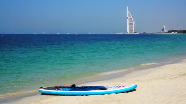 Dubaj, Spojené arabské emiráty - 20. ledna 2018. Surfovací prkno a Burj Hotel al Arab na pozadí. Vlny na pláži Al Sufouh. Moře. Perský záliv. — Stock video