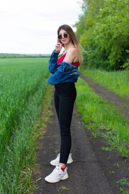  Güzel saçlı kot elbiseli bir kız yeşil bir tarlada duruyor. Yüzünde rüya gibi bir ifade var. Ilık bahar günü