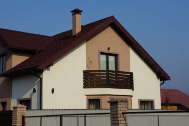  Kahverengi pencereli büyük bir ev ve mavi gökyüzüne karşı döşenmiş bir çatı.