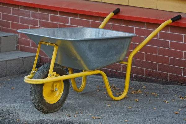 Gray Yellow Metal Wheelbarrow Stands Pavement Brick Wall — Stock fotografie