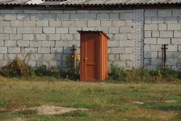 Red wooden toilet in the street in green grass against a gray brick wall — Stock Image Red Wooden Toilet Street Green Grass Gray Brick Wall Stock Photo