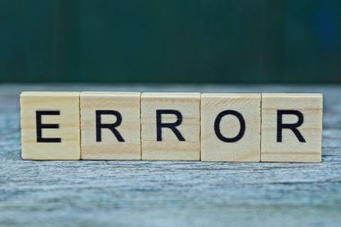 Kelime hatası, yeşil arkaplan üzerinde gri bir masa üzerindeki tahta harflerden kaynaklanıyor.