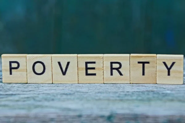 Parola Povertà Lettere Legno Tavolo Grigio Uno Sfondo Verde — Foto Stock