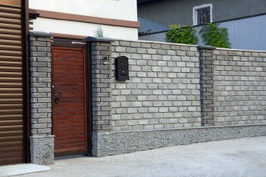 Kırsal bir sokakta kırmızı ahşap kapı ve gri tuğla çit